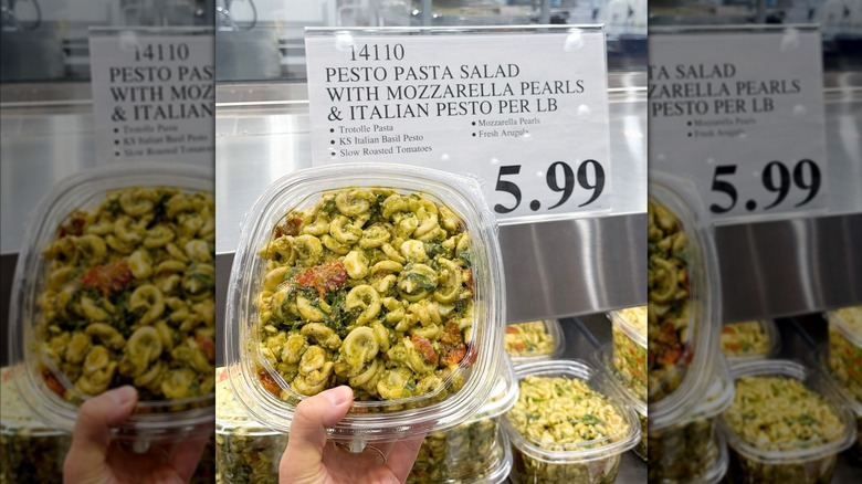 A hand holding a container of Costco's Pesto Pasta Salad.