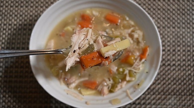Closeup of a full spoon over a bowl of Costco's Kirkland Rotisserie Chicken Noodle soup