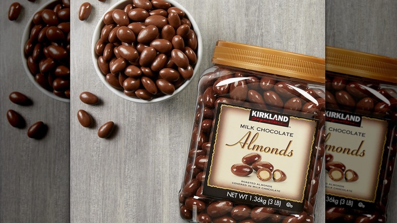 A bowl of chocolate nuts sits beside a large container of Kirkland Signature Milk Chocolate Almonds