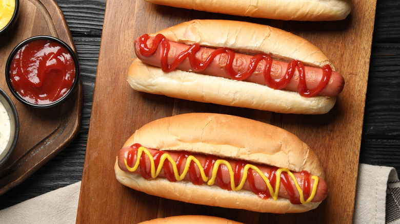 Hot dogs on wooden serving board dressed with mustard and ketchup