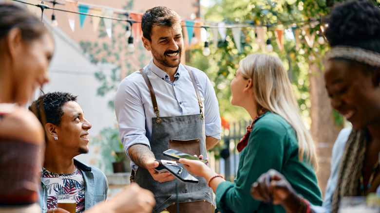 A server smiles while taking a customer's payment.
