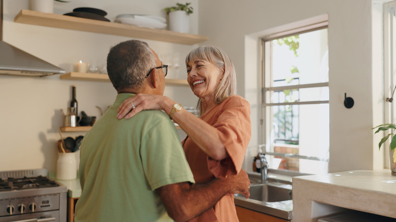 An elderly couple smiling and embracing in their kitchen