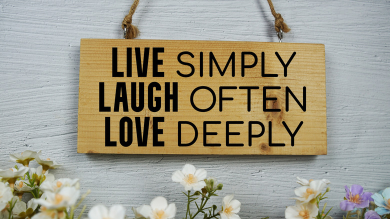 Wooden "live, laugh, love" sign hanging on a wall, flowers beneath it
