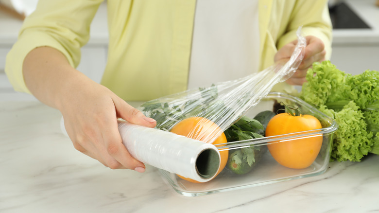 Woman putting plastic wrap over glass container with vegetables inside
