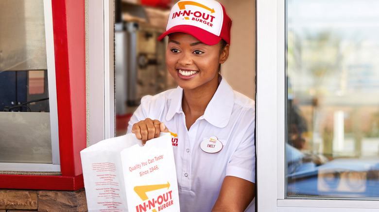 An In-N-Out employee holds a bag of food at a restaurant drive-thru window