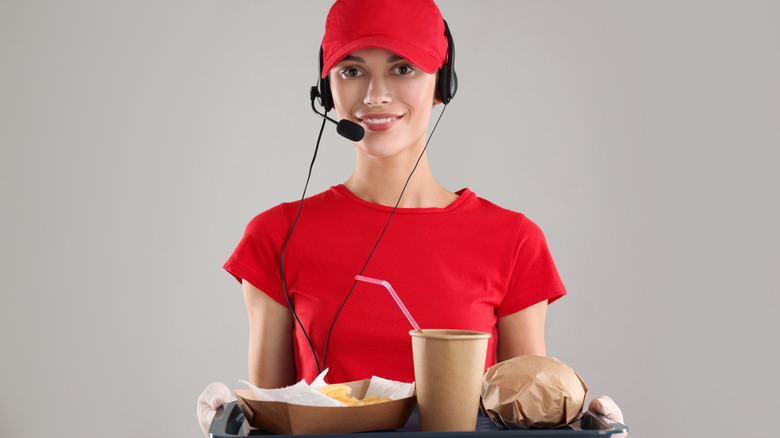 Fast-food worker in a red uniform wearing a headset and holding a food tray