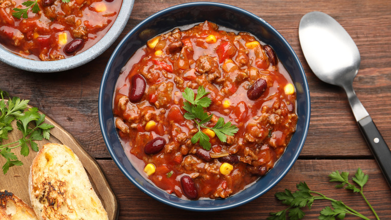 Chili with ground beef, beans, and corn in a blue bowl on a wooden surface