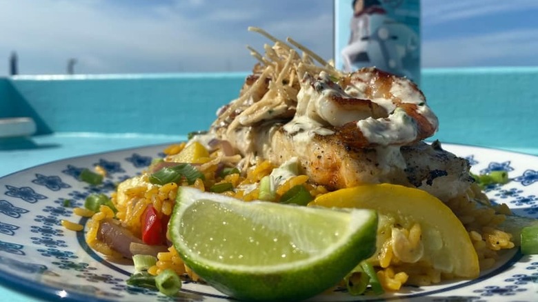 A seafood dish and bottle of craft spirits are shown on an outdoor table at Tide Tables Restaurant and Marina in Cortez, Florida