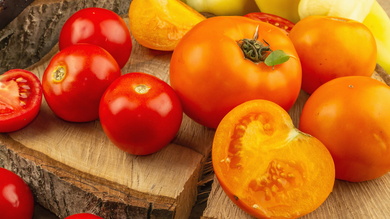Sliced and whole red and orange tomatoes on a wooden board