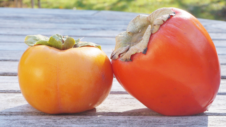 A fuyu and hachiya persimmon on a wooden surface
