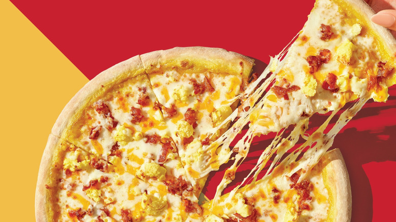 A hand pulls a slice of Casey's breakfast pizza away from the pie