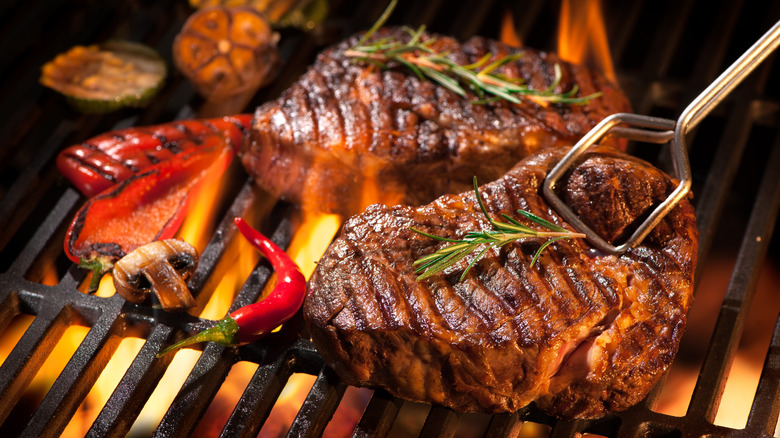 Two thick steaks barbecuing over flames.