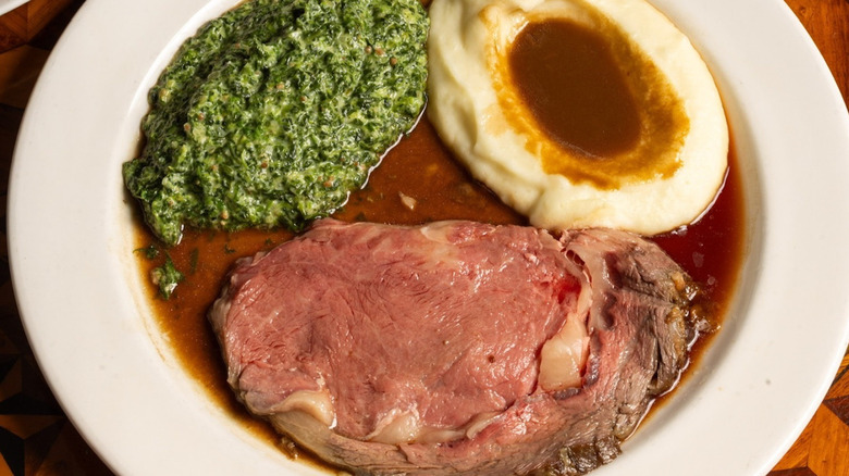 A piece of prime rib sits on a plate with mashed potatoes and creamed spinach.