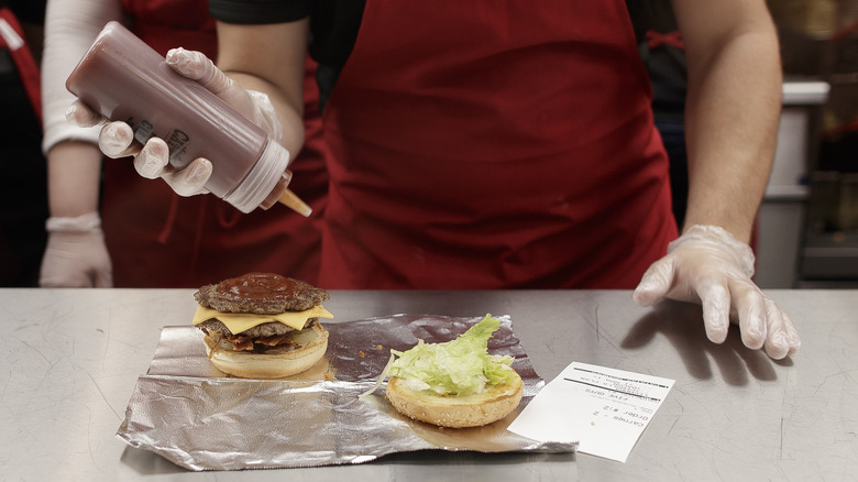 A Five Guys employee adding ketchup to a cooked burger