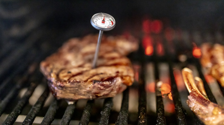 A pork chop on the grill with a meat thermometer in it