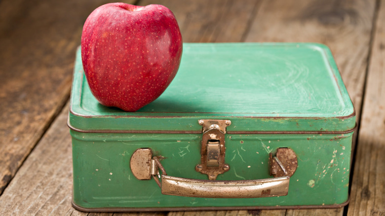 A green tin lunch box with an apple on top.