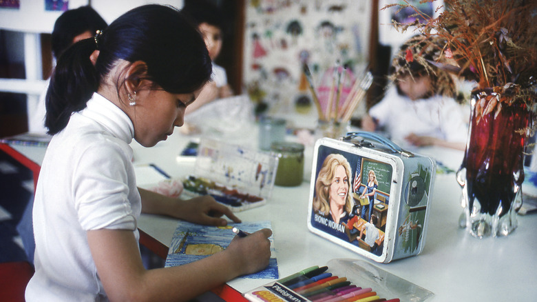 A child draws next to a Bionic Woman tin lunch box
