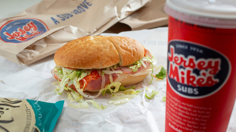 A small, unwrapped Jersey Mike's sub and drink.