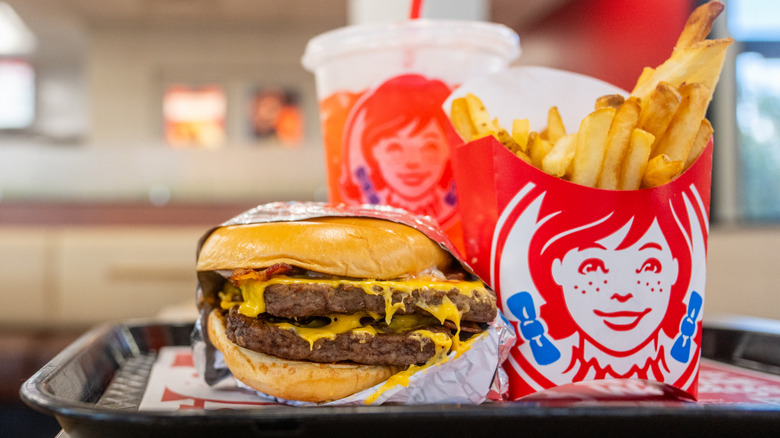 A Wendy's double-patty burger, french fries, and a drink sit on a tray inside a Wendy's restaurant