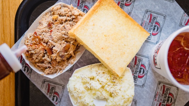 A plate of shredded pork, cornbread, mashed potatoes, with a soda and bottle of sauce from Skylight Inn BBQ