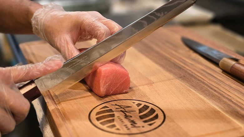 A chef slices raw fish on an Akami Sushi Bar cutting board