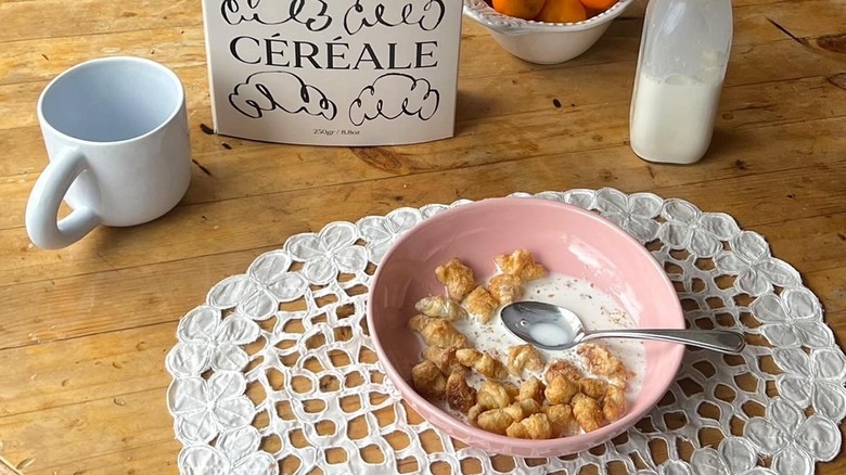 Mini croissants float in a bowl of milk with a spoon, next to an empty mug and a half-full bottle of milk.