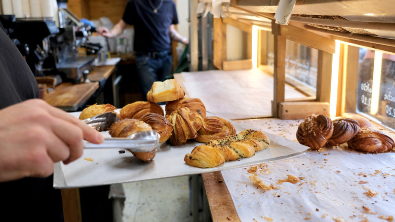 A hand uses tongs to place baked goods in a window