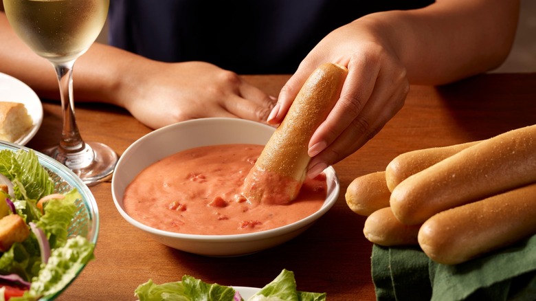 A diner dips a breadstick into a bowl of dipping sauce at Olive Garden.