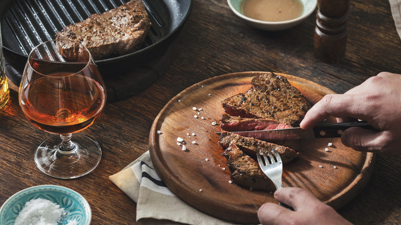 A diner enjoys steaks and a glass of whiskey at a restaurant table.