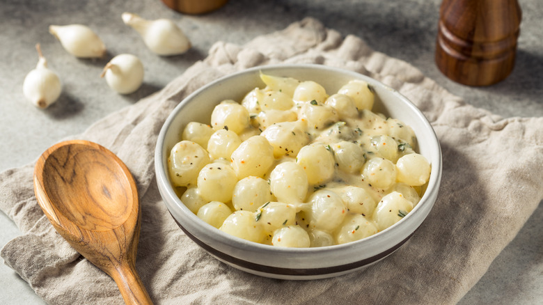 a bowl of creamed onions sits on a cloth napkin with a wooden spoon beside it
