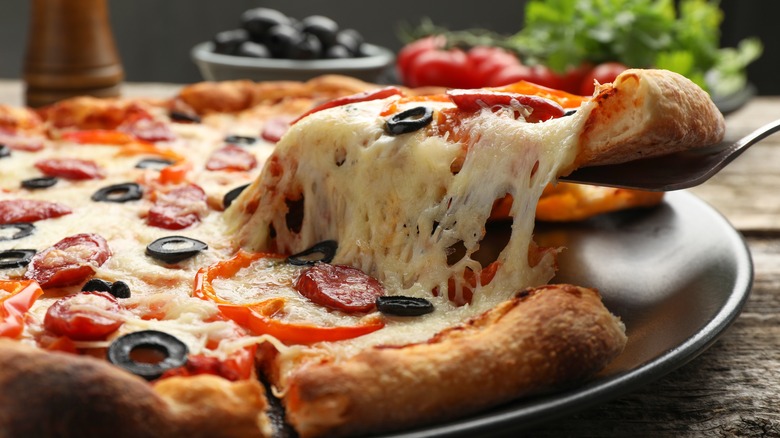 A slice of cheesy pizza is removed from a pan using a metal serving tool