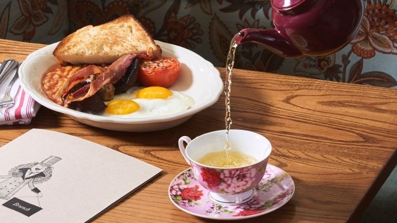 A small plate of breakfast and tea being poured in a teacup with The Dandelion's brunch menu on the table