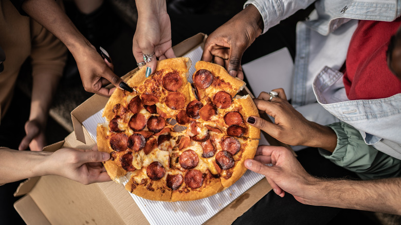 Multiple hands pull slices of pizza off the pie
