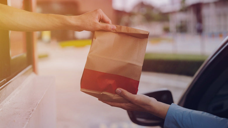 A hand reaches out with a fast food bag to a driver
