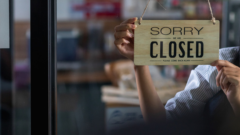 Hands hang a 'sorry we are closed' sign in a restaurant window