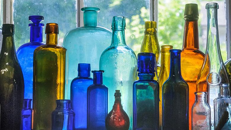 An assortment of antique glass bottles in different colors against a glass window, the light shining through them