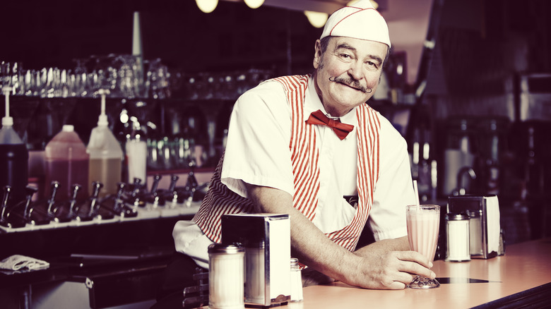 Soda fountain worker serving a strawberry milkshake