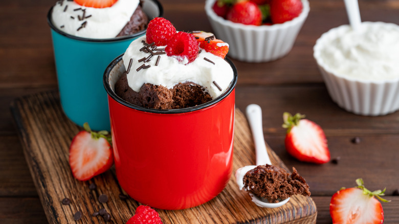 chocolate mug cakes in colorful mugs with whipped cream and berries