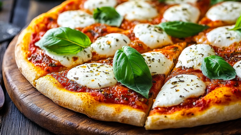 Sliced margherita pizza with fresh basil on a wooden board.