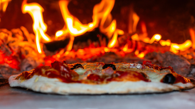 Pepperoni pizza in a wood-fire oven with fire in the background.