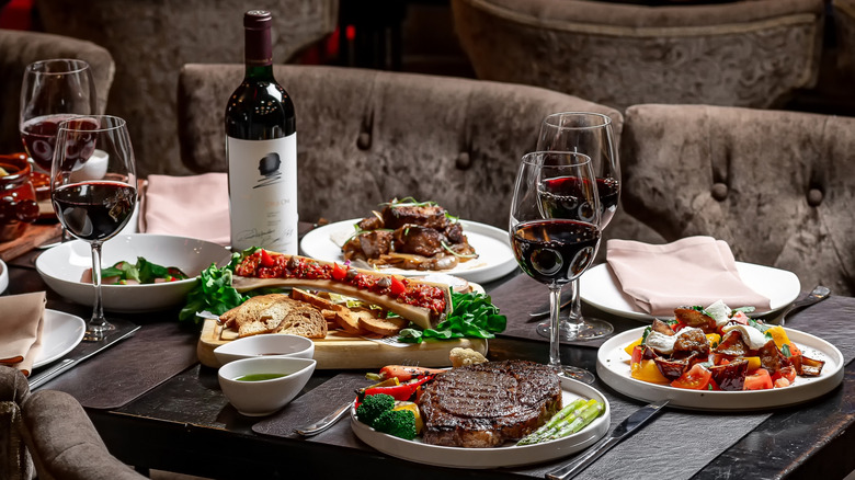 Steak and other dishes with glasses of red wine on a restaurant table
