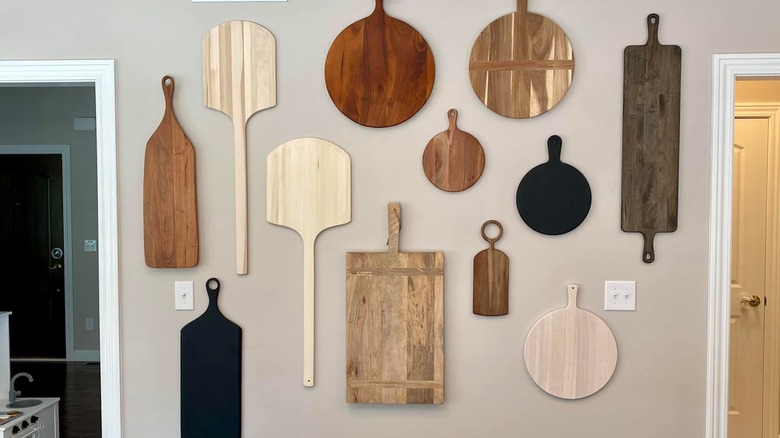 Cutting boards hang on a beige kitchen wall in an arranged fashion