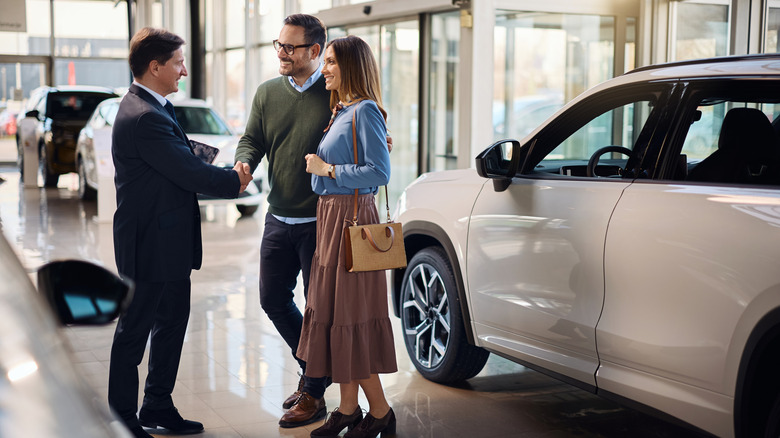A couple shaking hands with an employee at a car dealership.