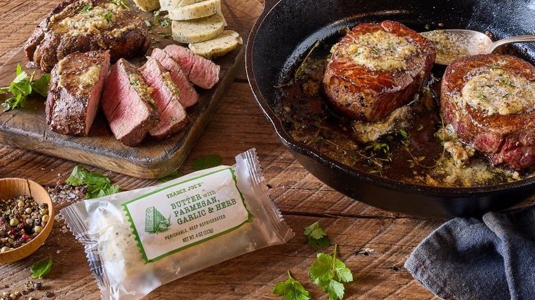 Trader Joe's Butter with Parmesan, Garlic & Herb next to two steaks in a pan with butter on top and sliced steak and butter on a board