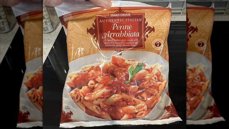 Someone holds up a bag of Trader Joe's penne arrabbiata