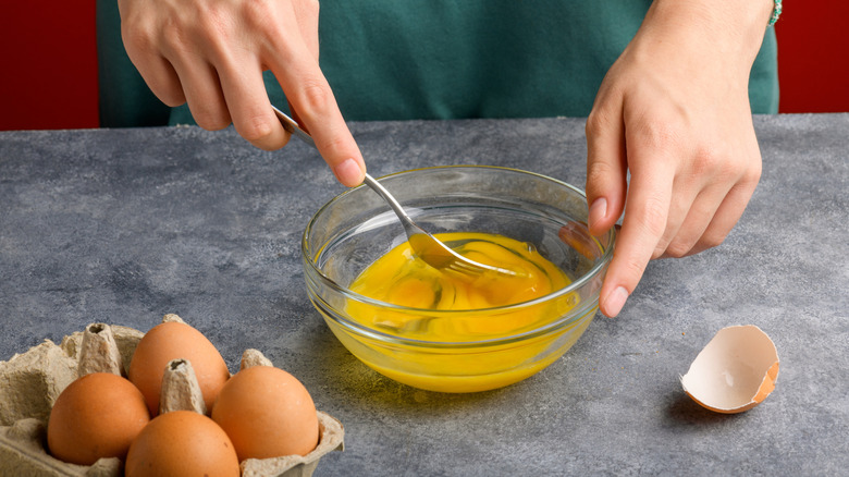 A person mixing eggs with a fork.