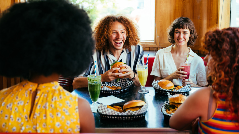 A group of friends eat burgers and drink smoothies at a fast food booth