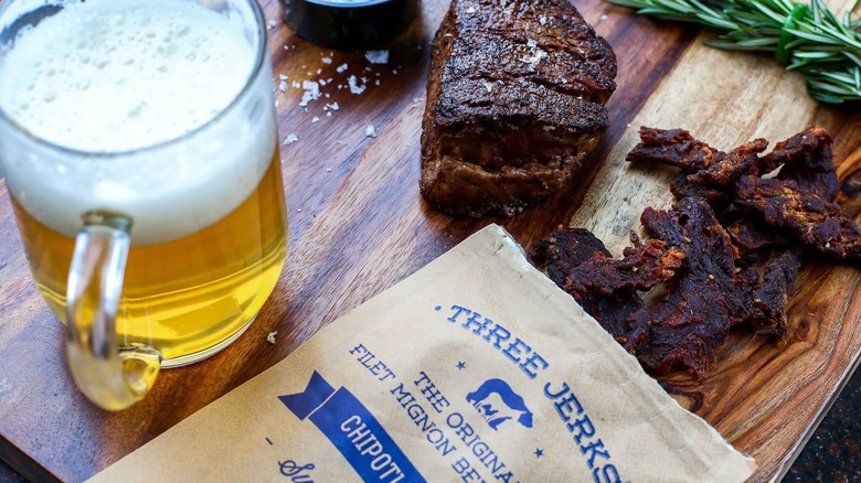 Three Jerks Jerky jerky on a wooden board with a beer