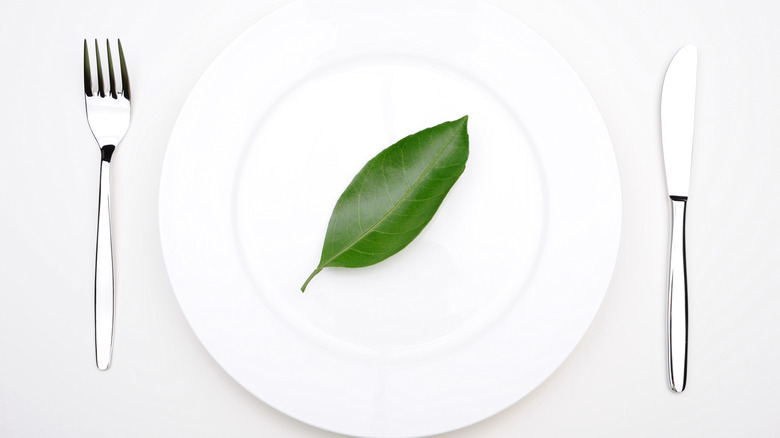 A single leaf sits on a white plate, flanked by knife and forl