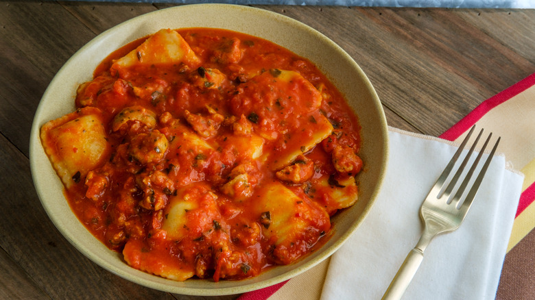 A bowl of ravioli in a red sauce with sausage